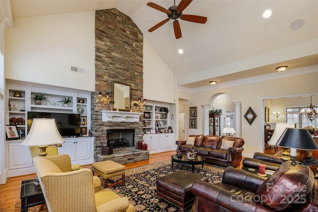 living room featuring a stone fireplace, high vaulted ceiling, built in shelves, light wood-type flooring, and ornate columns