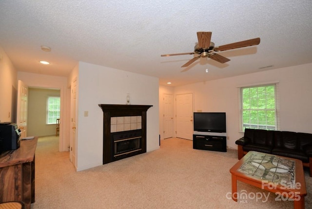 living room featuring light colored carpet, a textured ceiling, a tile fireplace, and a wealth of natural light