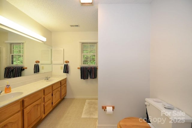 bathroom featuring a healthy amount of sunlight, toilet, vanity, and a textured ceiling