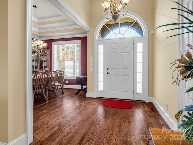 foyer entrance with ornamental molding, dark hardwood / wood-style floors, a notable chandelier, and a tray ceiling