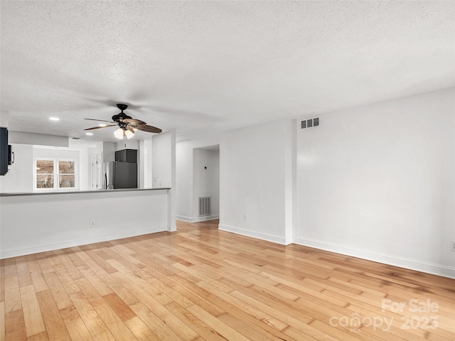 unfurnished living room featuring visible vents, a ceiling fan, a textured ceiling, light wood-type flooring, and baseboards