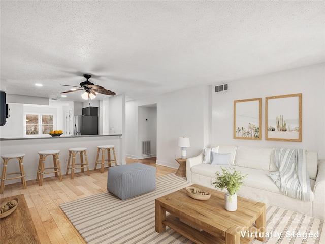 living area with a textured ceiling, ceiling fan, light wood-style flooring, and visible vents