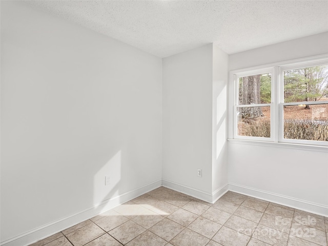 empty room featuring a textured ceiling, light tile patterned floors, and baseboards