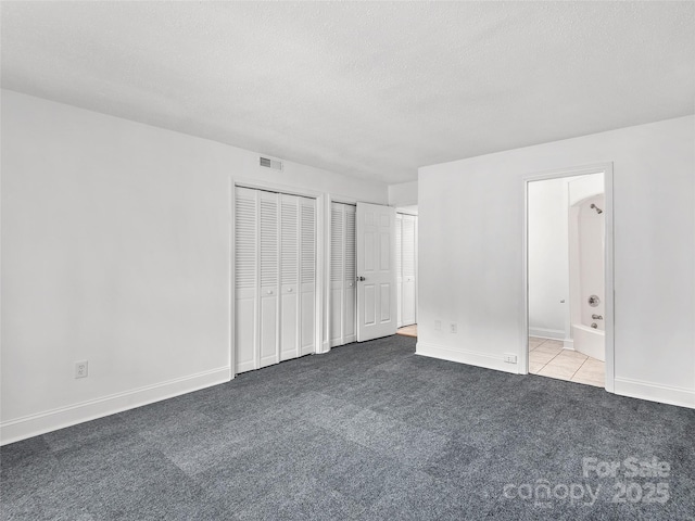 unfurnished bedroom with a textured ceiling, light carpet, visible vents, baseboards, and multiple closets