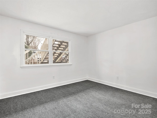 unfurnished room with a textured ceiling, dark carpet, and baseboards