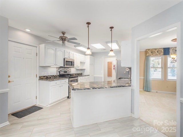 kitchen with dark stone counters, a peninsula, appliances with stainless steel finishes, a skylight, and white cabinets