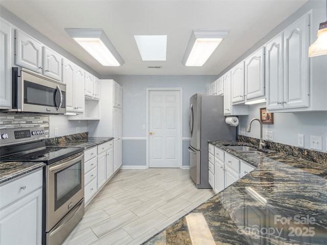 kitchen with a sink, dark stone counters, white cabinets, and stainless steel appliances