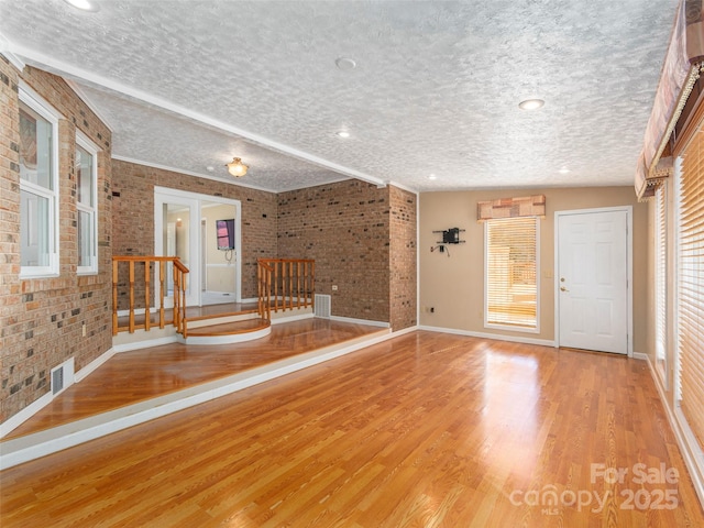 interior space featuring light wood finished floors, visible vents, brick wall, baseboards, and a textured ceiling