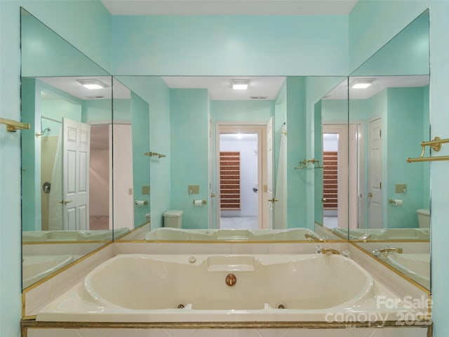 bathroom featuring toilet, a tub with jets, and a sink