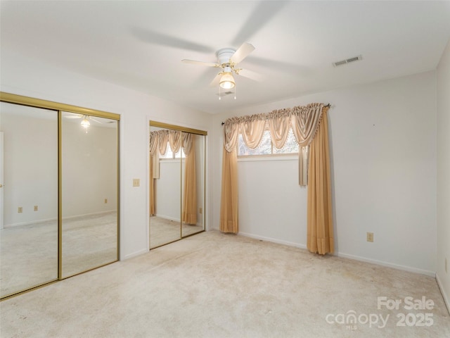 unfurnished bedroom with visible vents, two closets, baseboards, ceiling fan, and carpet flooring