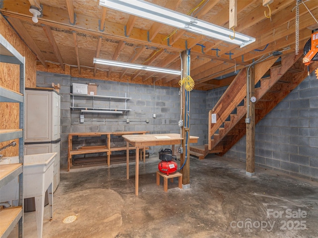 unfinished basement featuring stairway, a workshop area, and concrete block wall