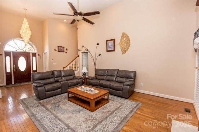 living room with hardwood / wood-style floors, ceiling fan with notable chandelier, and a high ceiling