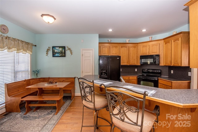 kitchen featuring a breakfast bar area, backsplash, black appliances, light hardwood / wood-style floors, and kitchen peninsula