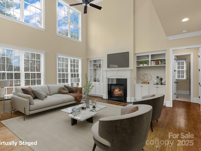 living room with built in shelves, a towering ceiling, ceiling fan, and hardwood / wood-style flooring