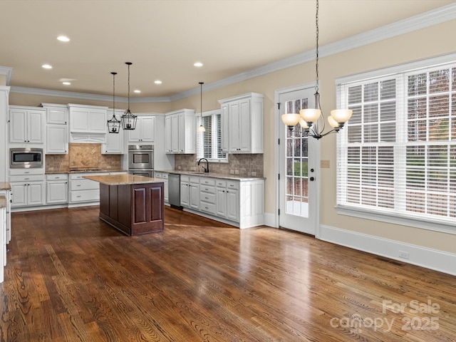 kitchen with appliances with stainless steel finishes, decorative light fixtures, white cabinetry, sink, and a center island