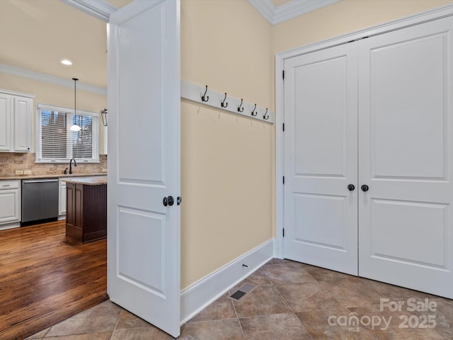 mudroom with crown molding, sink, and light tile patterned flooring