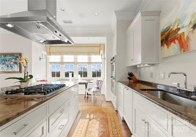 kitchen with sink, island range hood, dark stone counters, stainless steel appliances, and white cabinets