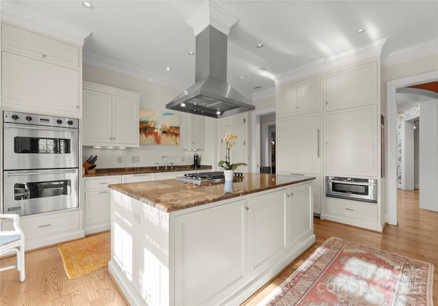 kitchen with island exhaust hood, appliances with stainless steel finishes, a center island, and white cabinets