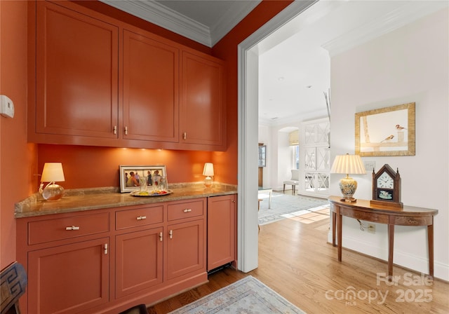 bar featuring light stone countertops, ornamental molding, and light hardwood / wood-style floors