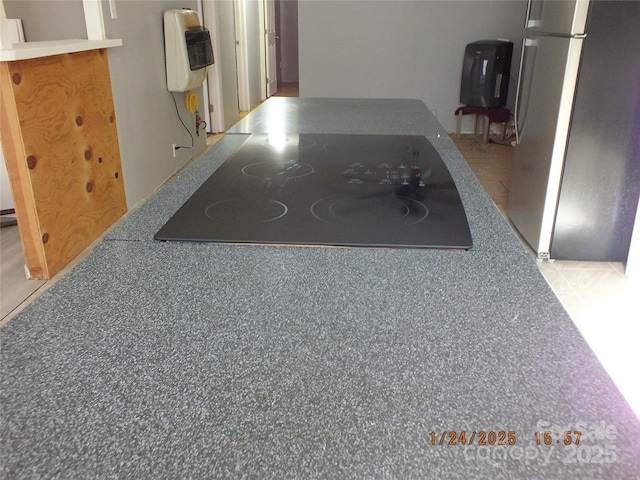 interior space featuring heating unit, black electric stovetop, and stainless steel refrigerator