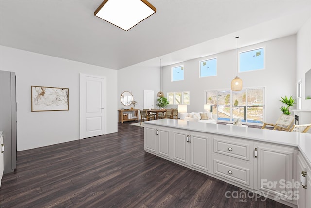 kitchen with white cabinetry, hanging light fixtures, stainless steel fridge, dark hardwood / wood-style flooring, and a high ceiling