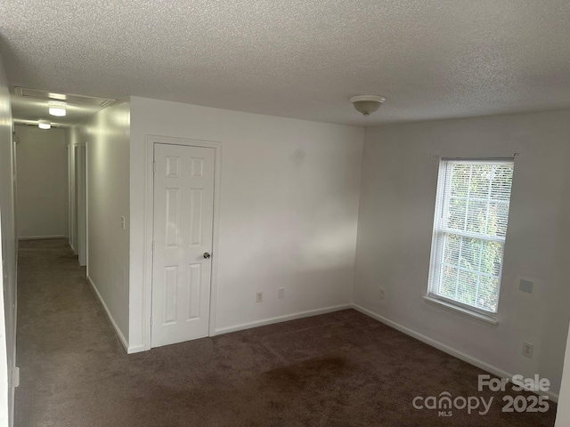 empty room with dark carpet and a textured ceiling