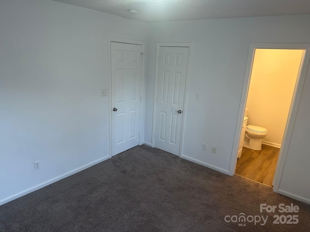 unfurnished bedroom featuring dark colored carpet and ensuite bathroom