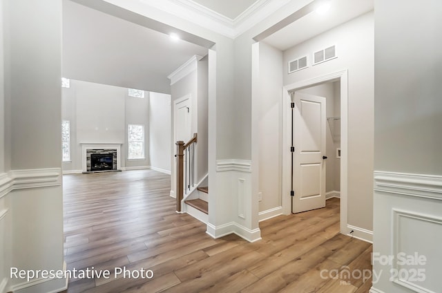 foyer with light wood-style flooring, visible vents, stairs, ornamental molding, and a glass covered fireplace