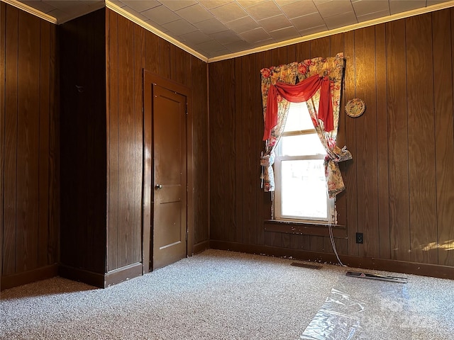 spare room with crown molding, wooden walls, and carpet