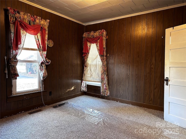 carpeted spare room with ornamental molding and wood walls