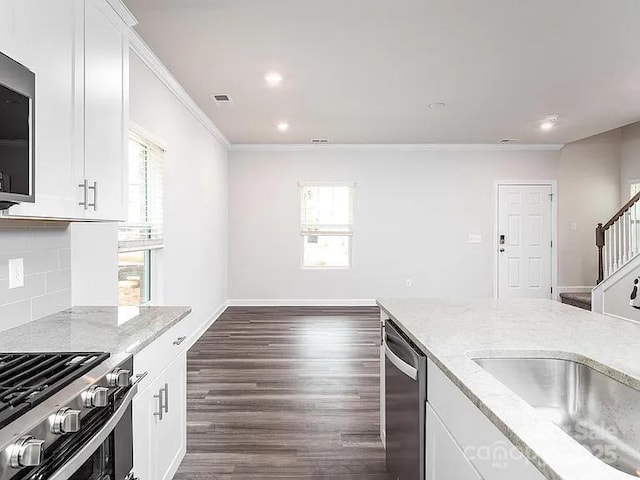 kitchen featuring appliances with stainless steel finishes, a wealth of natural light, white cabinets, backsplash, and light stone counters