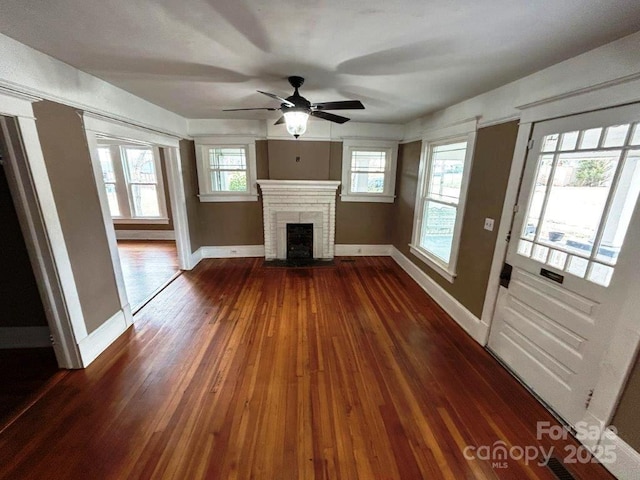 unfurnished living room featuring dark wood-style floors, a brick fireplace, and baseboards