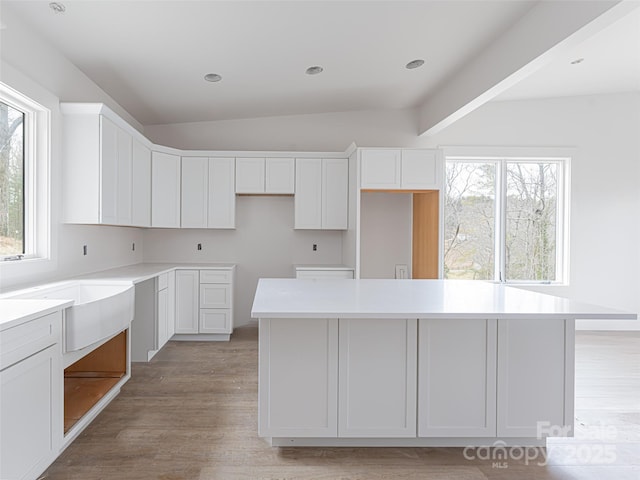 kitchen featuring lofted ceiling, sink, white cabinetry, a center island, and light wood-type flooring