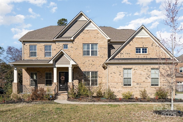 view of front of home featuring covered porch, a shingled roof, a front lawn, and brick siding