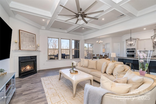 living area featuring wood finished floors, beamed ceiling, coffered ceiling, and a glass covered fireplace