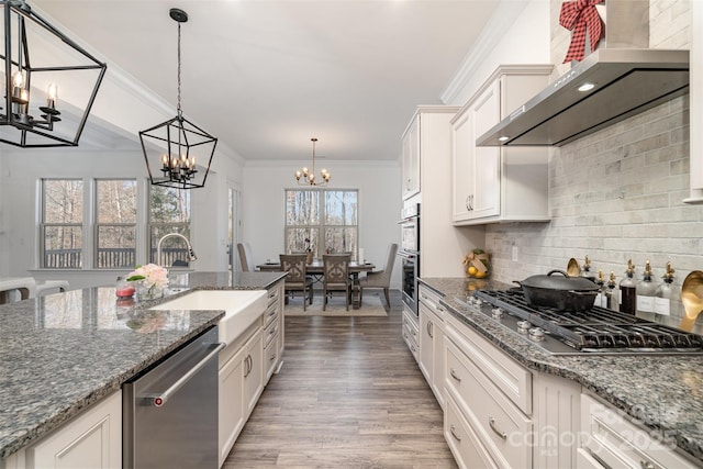 kitchen with a sink, white cabinetry, hanging light fixtures, appliances with stainless steel finishes, and wall chimney exhaust hood