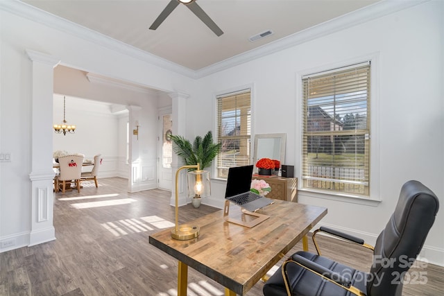 home office featuring ceiling fan with notable chandelier, wood finished floors, visible vents, ornamental molding, and decorative columns