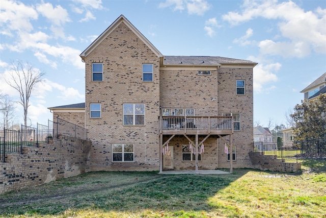 rear view of house with a deck, brick siding, a lawn, and fence