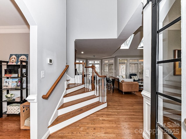 stairs featuring hardwood / wood-style floors, crown molding, and a skylight