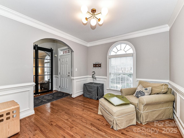 sitting room with hardwood / wood-style floors, crown molding, and a notable chandelier