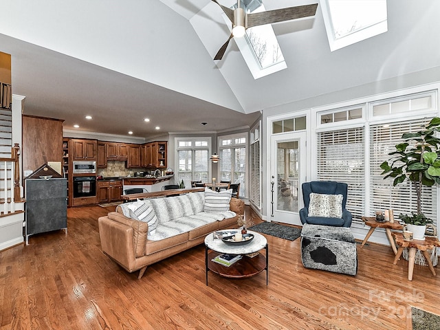 living room with crown molding, high vaulted ceiling, a skylight, and hardwood / wood-style floors