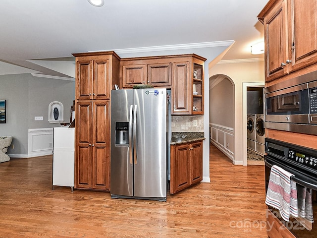 kitchen featuring appliances with stainless steel finishes, dark stone countertops, ornamental molding, light hardwood / wood-style floors, and washing machine and dryer