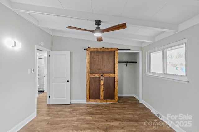 unfurnished bedroom with hardwood / wood-style floors, lofted ceiling with beams, ceiling fan, a barn door, and a closet