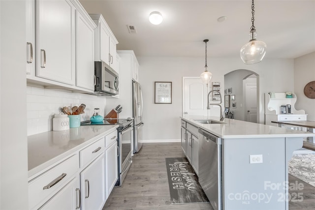 kitchen featuring sink, appliances with stainless steel finishes, a kitchen island with sink, white cabinets, and decorative light fixtures