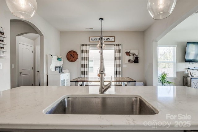 kitchen with light stone counters, sink, and decorative light fixtures