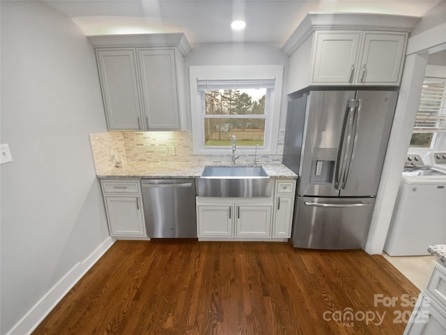 kitchen with appliances with stainless steel finishes, tasteful backsplash, sink, light stone counters, and dark wood-type flooring