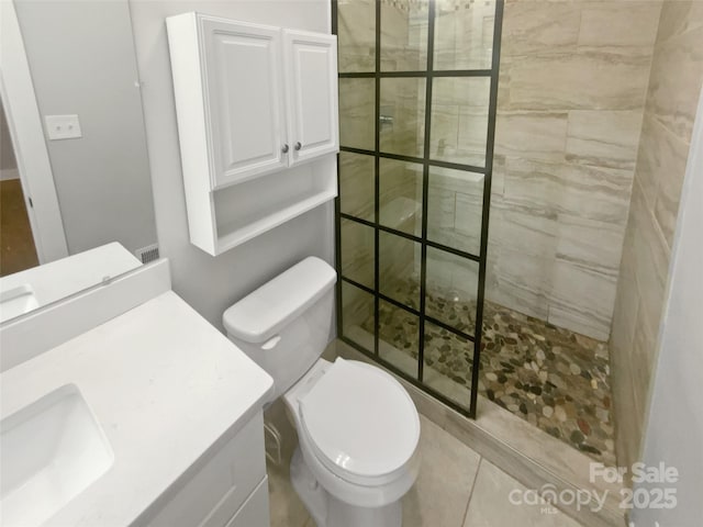 bathroom featuring vanity, a tile shower, tile patterned floors, and toilet