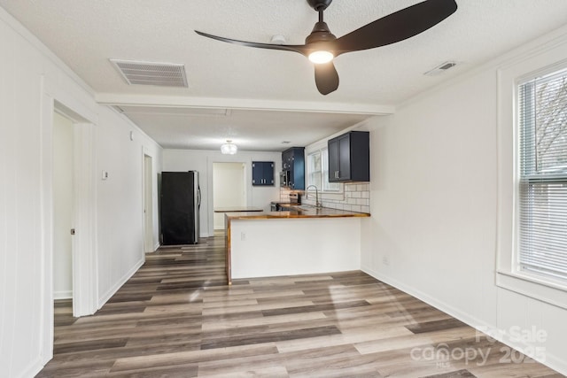 kitchen featuring sink, wooden counters, stainless steel refrigerator, decorative backsplash, and kitchen peninsula