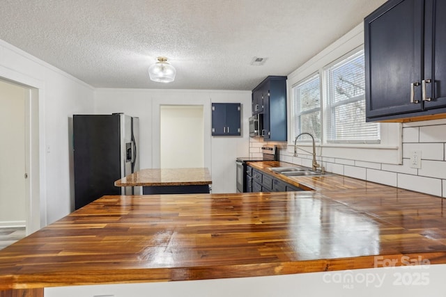 kitchen featuring sink, blue cabinetry, stainless steel appliances, a textured ceiling, and wood counters