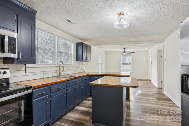 kitchen with appliances with stainless steel finishes, tasteful backsplash, blue cabinets, sink, and a center island